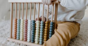 A young child engaging in learning with a wooden abacus on a carpet, emphasizing early education.